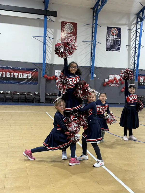 NECA cheerleaders in uniform posing together in the school gym.