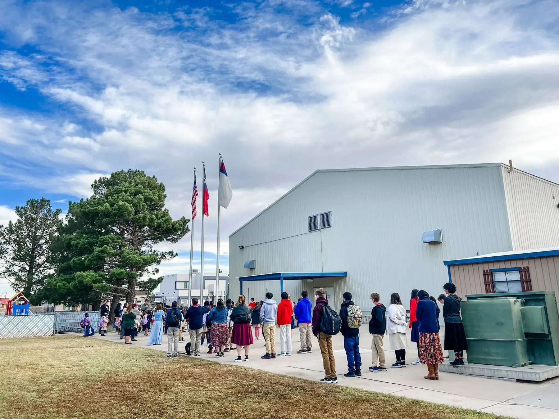 NECA students standing in lines outside the school building during a morning flag ceremony with the American, Texas and Christian flags.