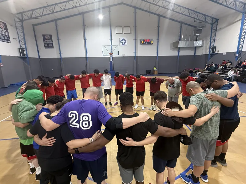 NECA basketball players gathered in a wide huddle on the gym floor.