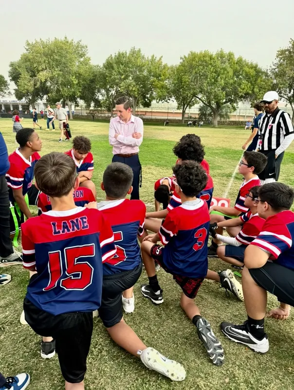A NECA flag football team kneeling in a circle on the field while a coach talks.
